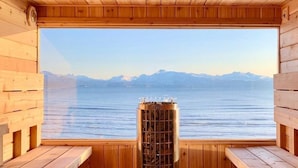 A sauna room with wooden benches and a large window overlooking a body of water and mountains. - Homer Inn and Spa (Homer)