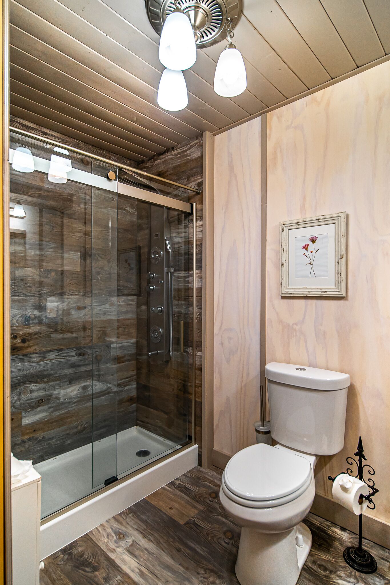 A bathroom with a glass-enclosed shower, a white toilet, and a framed picture on the wall.