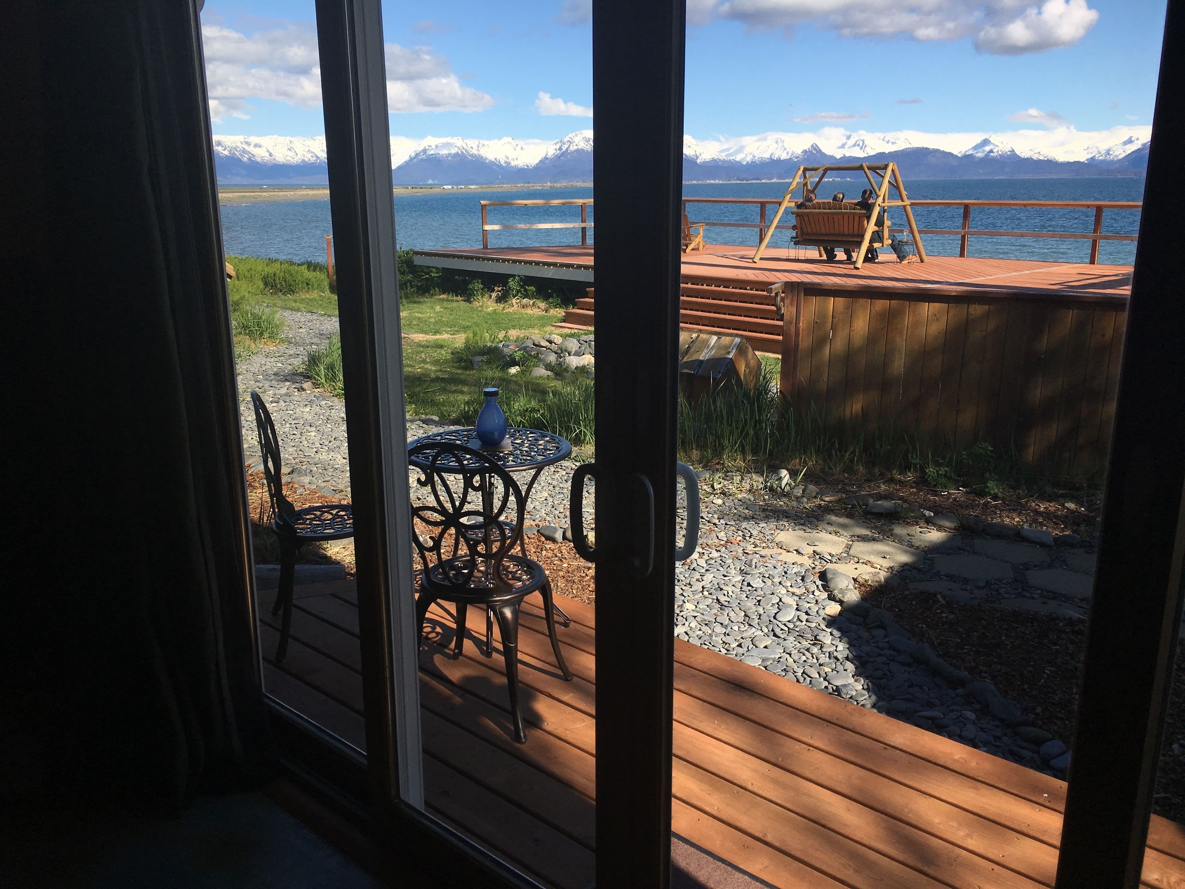 A wooden deck with outdoor furniture, a swing, and a view of a lake with mountains in the background.