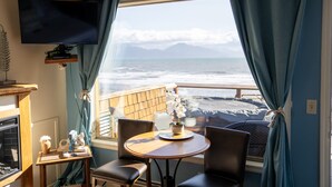 A room with a wooden table and chairs, a television mounted on the wall, and a view of the ocean through large windows with curtains. - Homer Inn and Spa (Homer)