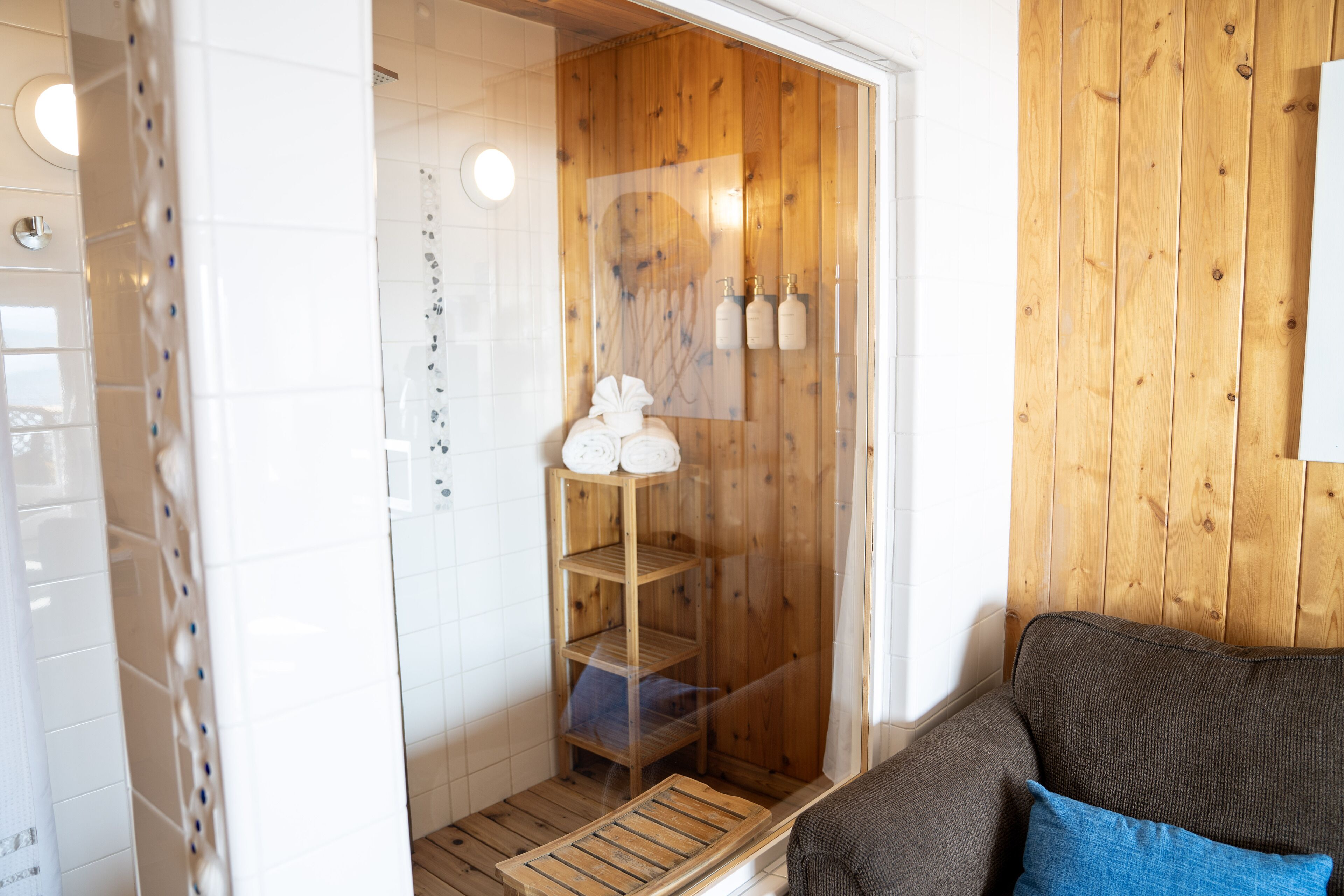 Un bagno con cabina doccia in legno, un porta asciugamani e uno scaffale con bottiglie.