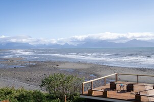 A wooden deck with two chairs and a table overlooking a rocky beach and ocean.