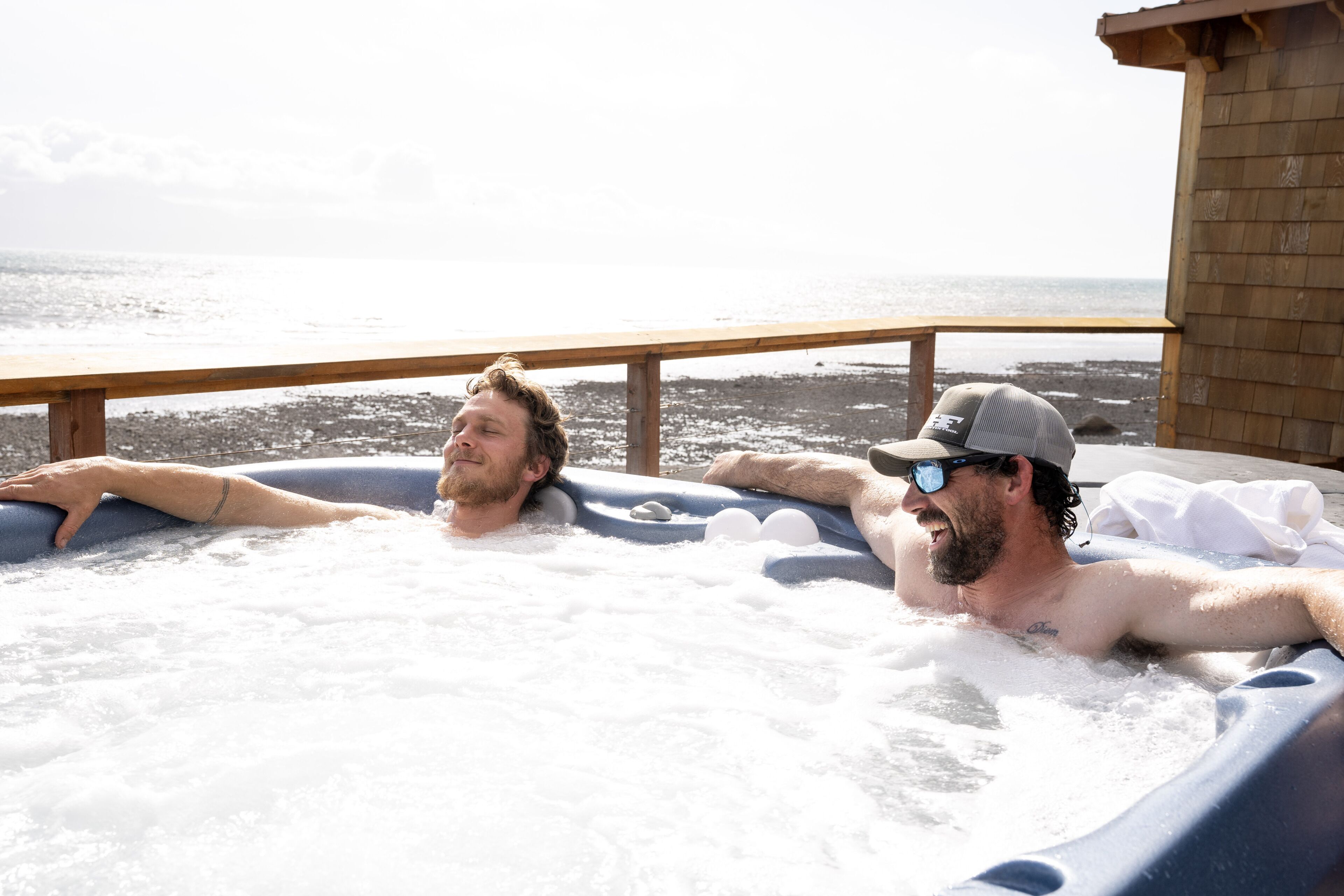 Two people relaxing in a hot tub with a wooden deck and a view of the sea.