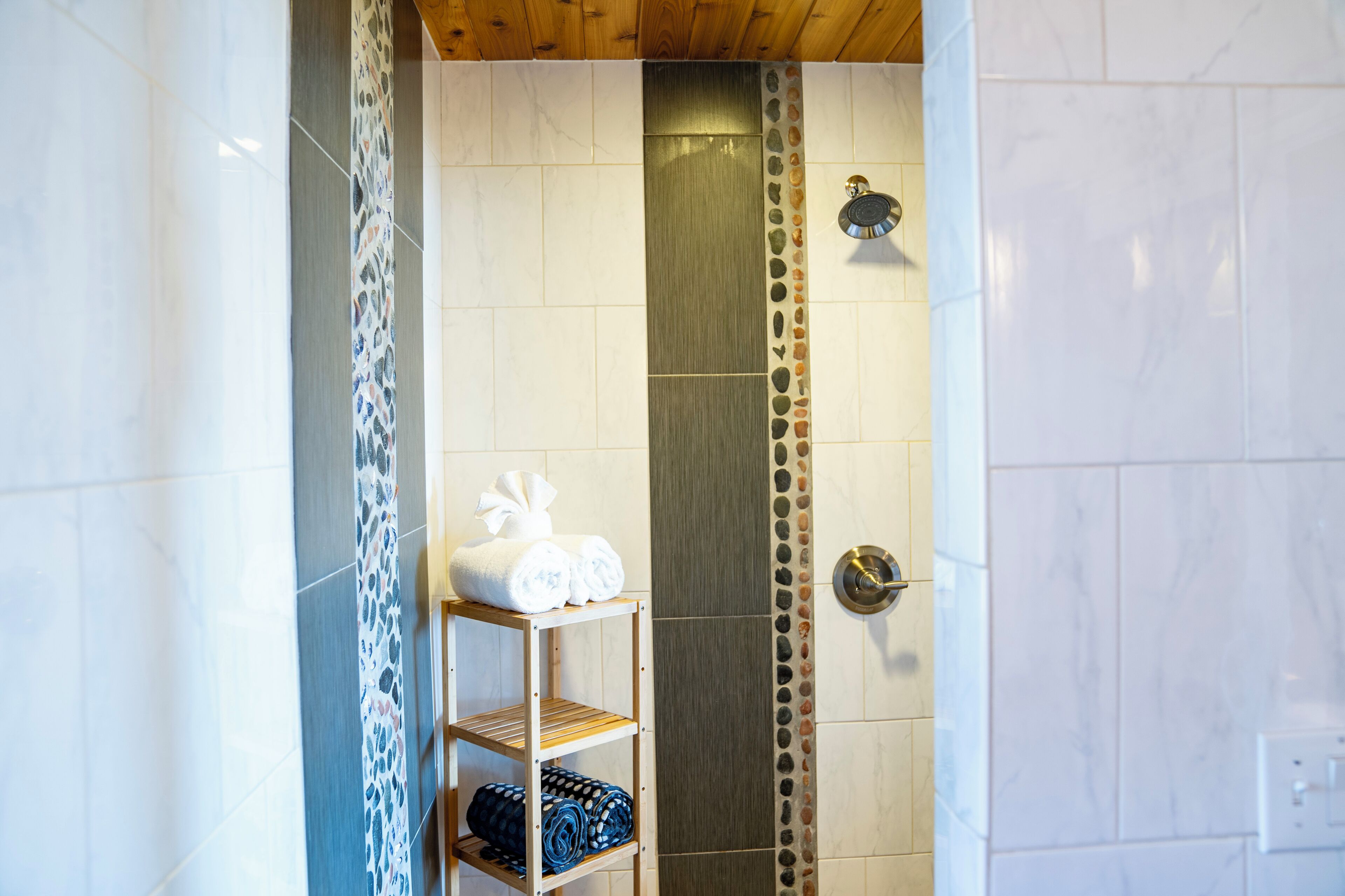 A bathroom with a shower, a shelf with towels, and a decorative tile border.