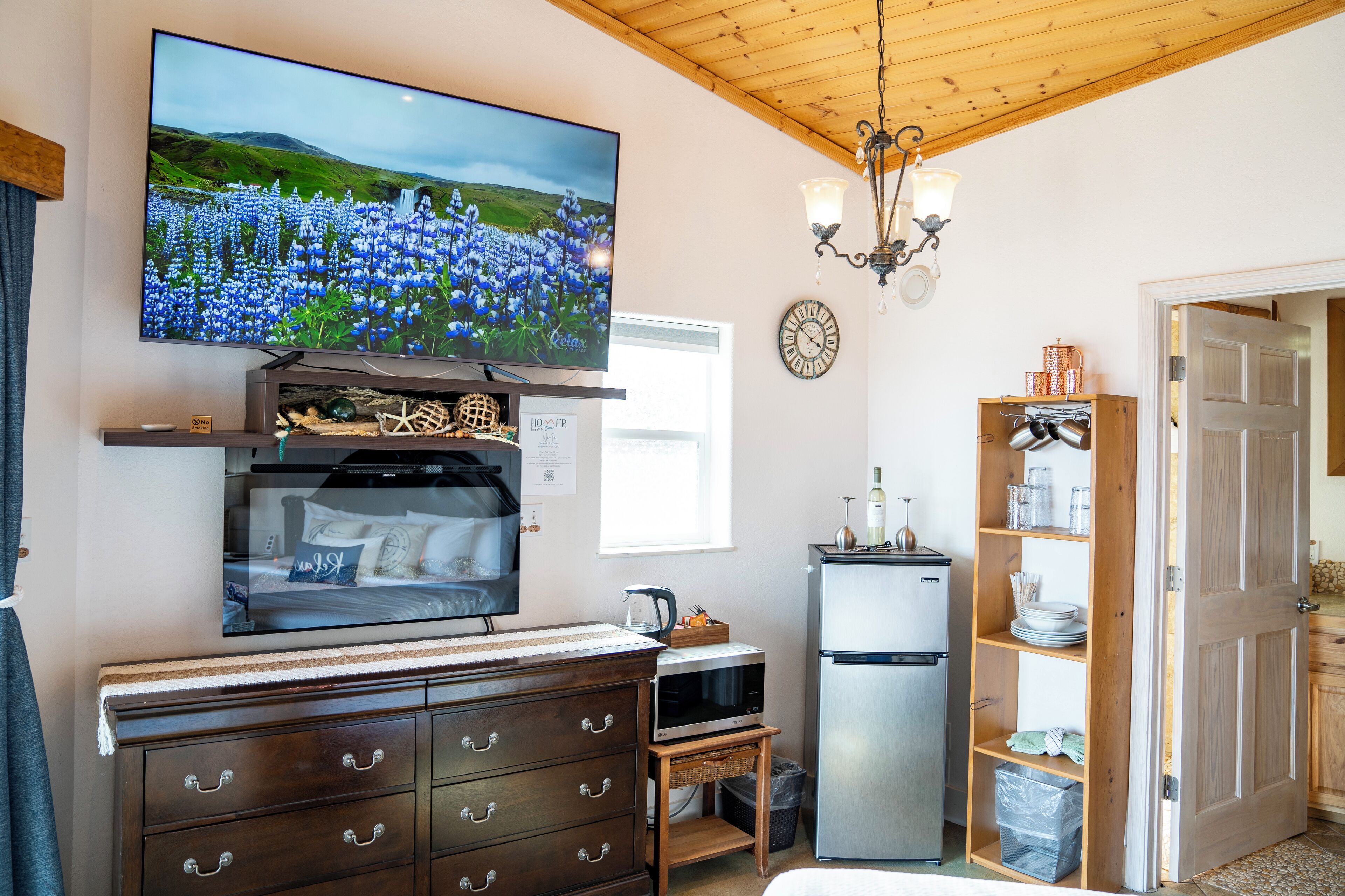 A cozy room with a TV, wooden dresser, microwave, refrigerator, and a small kitchen area.