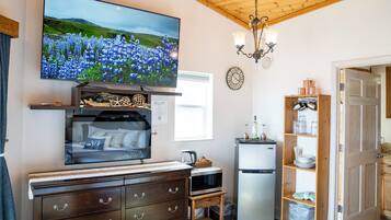 A cozy room with a TV, wooden dresser, microwave, refrigerator, and a small kitchen area.