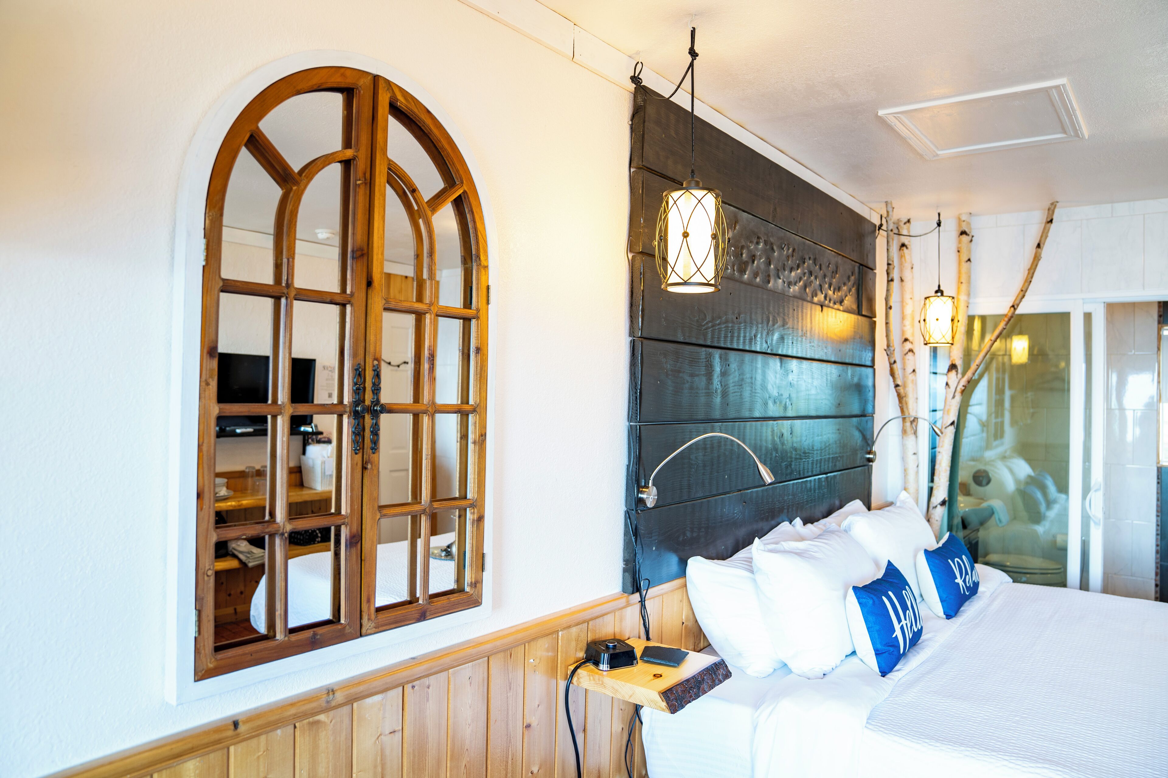 Quarto com cabeceira de madeira, uma grande janela em arco e mesa de cabeceira com abajur.