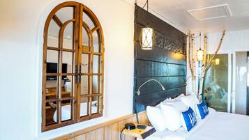 Quarto com cabeceira de madeira, uma grande janela em arco e mesa de cabeceira com abajur.