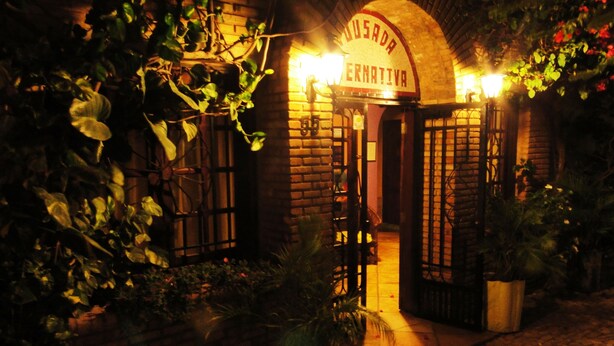 A brick building with a sign reading "Usada Alternativa" at the entrance, surrounded by greenery and potted plants. - Pousada Alternativa (Aracati)