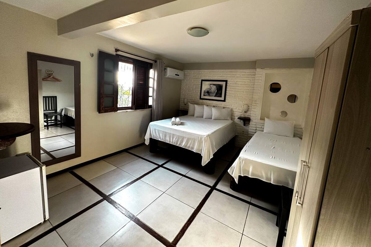 A hotel room with two beds, a desk, a chair, a window with curtains, and a picture on the wall.