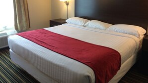 A hotel room with a bed, a nightstand, a wall-mounted lamp, and a window with curtains. - The Inn Forza (Monaca)