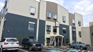 A multi-story building with a sign reading "The Inn." There are parking spaces in front, and a BMW SUV is parked. - The Inn Forza (Monaca)