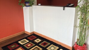 A reception area with a white counter, a patterned rug, a potted plant, and a telephone. - The Inn Forza (Monaca)