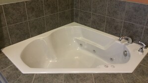 A white freestanding bathtub with a single faucet and a control knob, set against a tiled wall with a mix of gray and beige tiles. - The Inn Forza (Monaca)