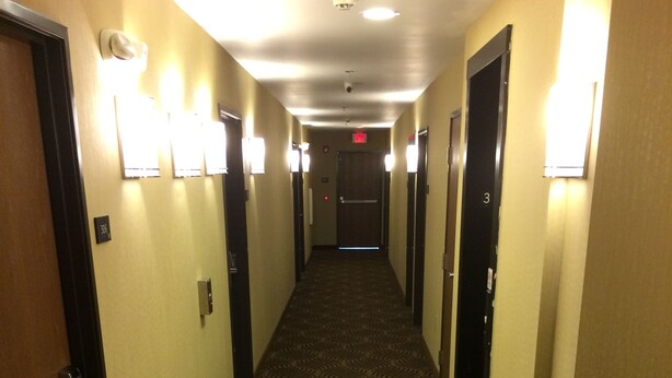 A hotel hallway with patterned carpet, doors, and wall-mounted lights. - The Inn Forza (Monaca)