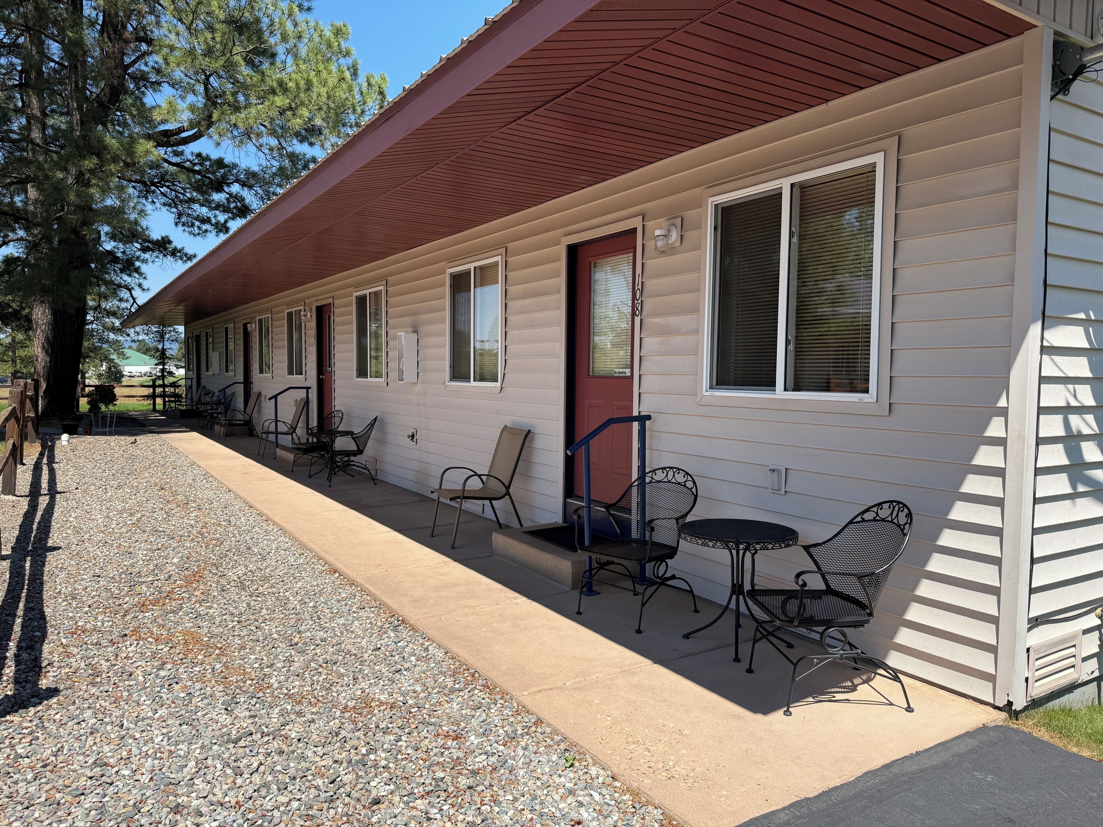 Un motel con patio cubierto, mobiliario exterior y camino de entrada de grava.