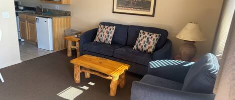 A compact living space with a kitchenette, a sofa, a coffee table, and a lamp.