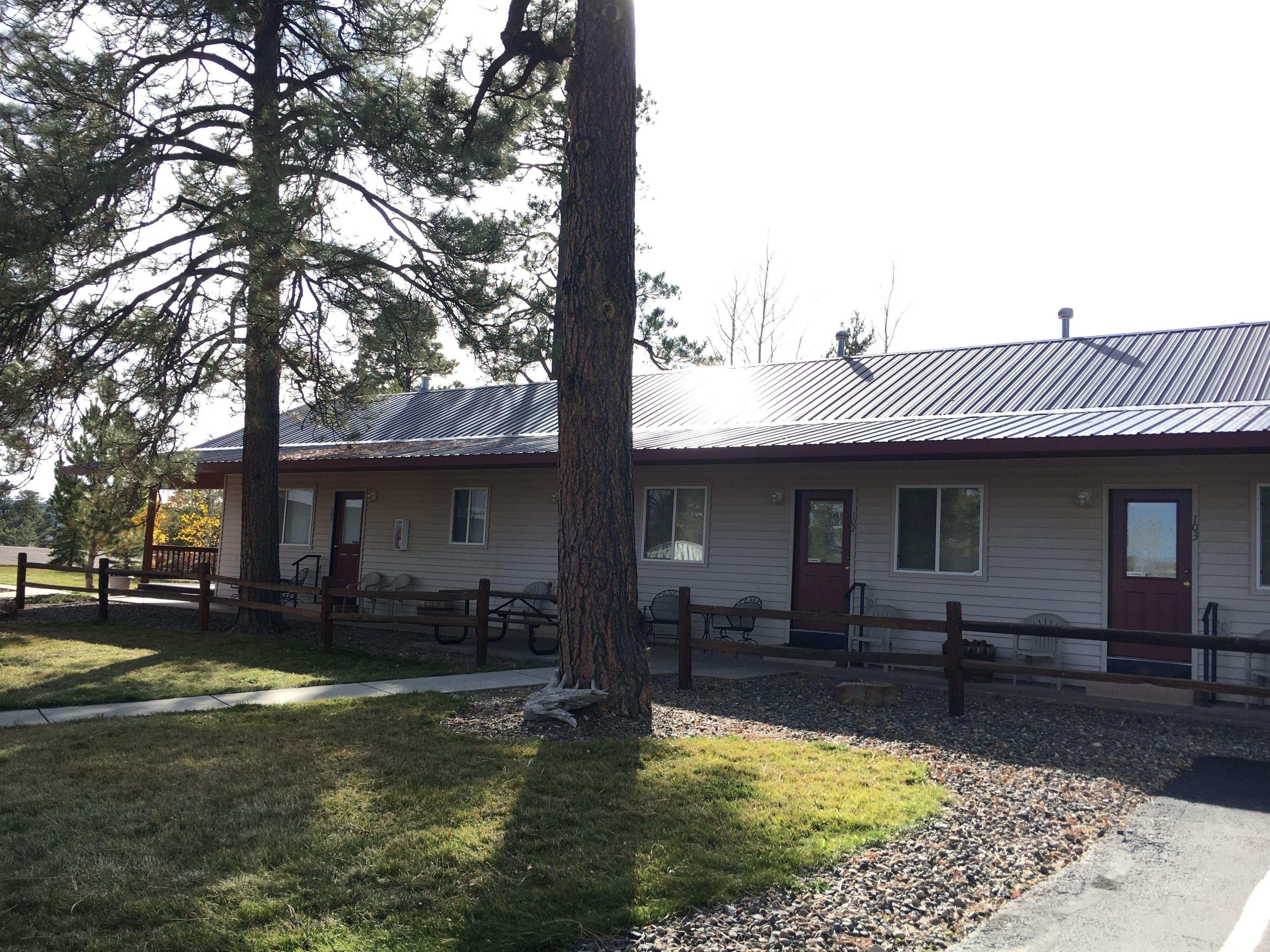 A single-story building with a metal roof, a front porch with benches, and a gravel driveway.