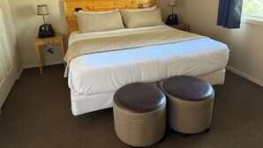 Un dormitorio ordenado con una cama grande, dos mesitas de noche, una obra de arte colgada en la pared y una ventana con cortinas.