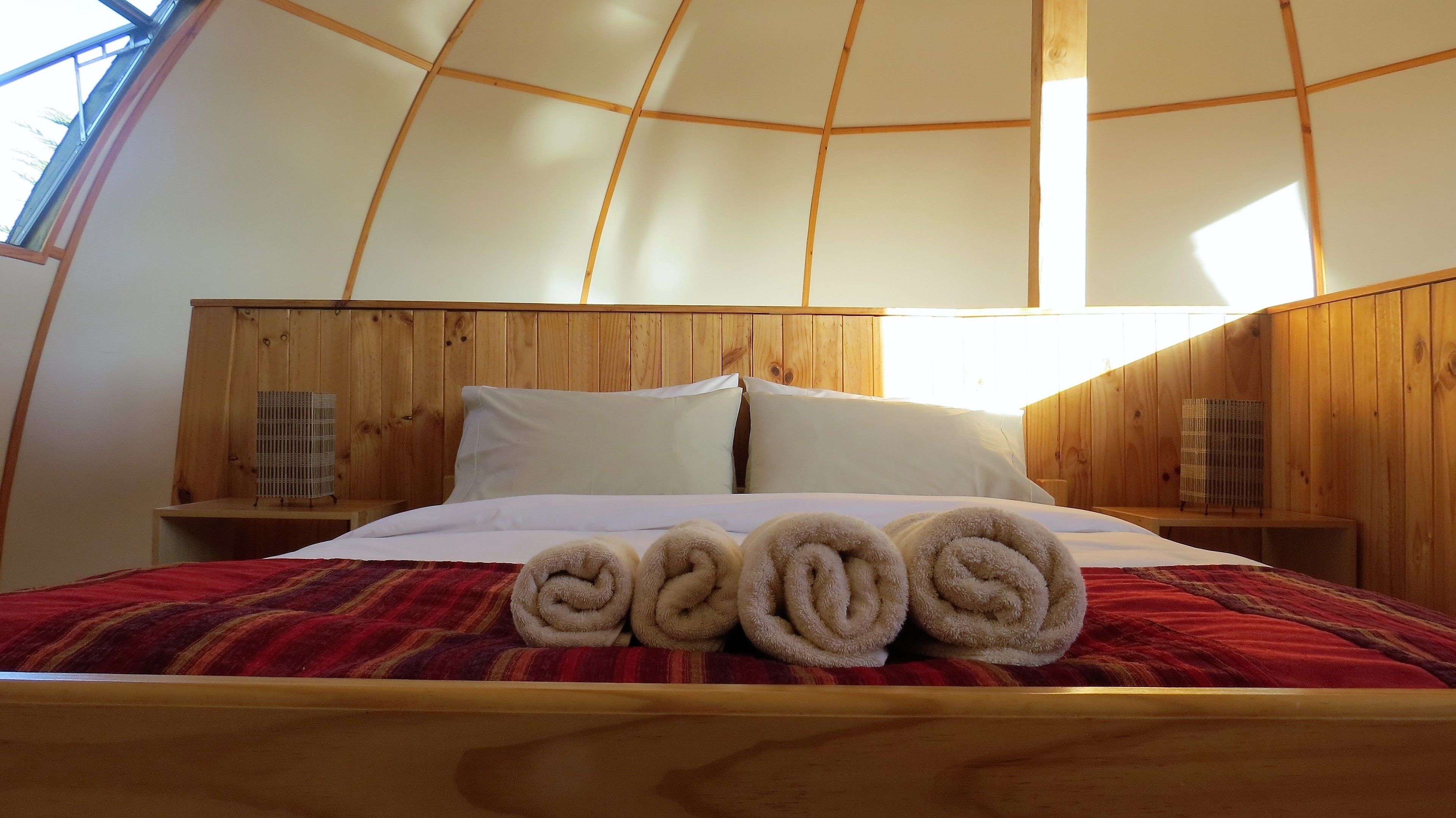 Ein gemütliches Zimmer mit einem hölzernen Kopfteil, einem Bett mit weißer Bettwäsche und zusammengerollten Handtüchern auf dem Bett.