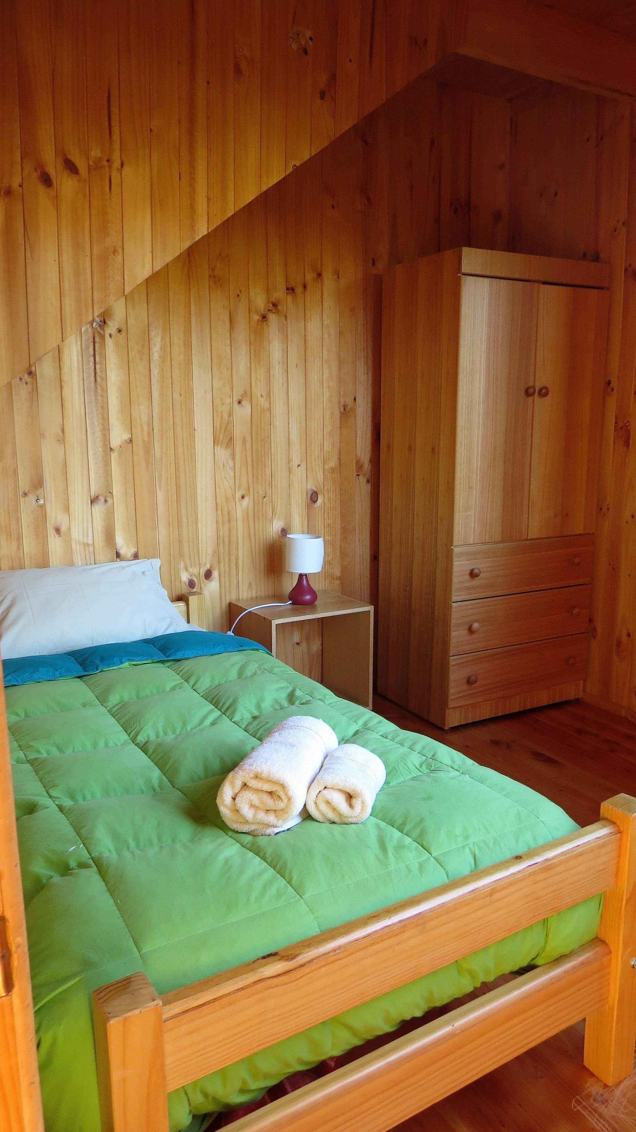 Una habitación con paneles de madera, una cama, una mesita de noche y un armario.