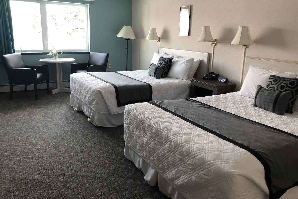 A hotel room with two beds, a desk, chairs, and lamps.