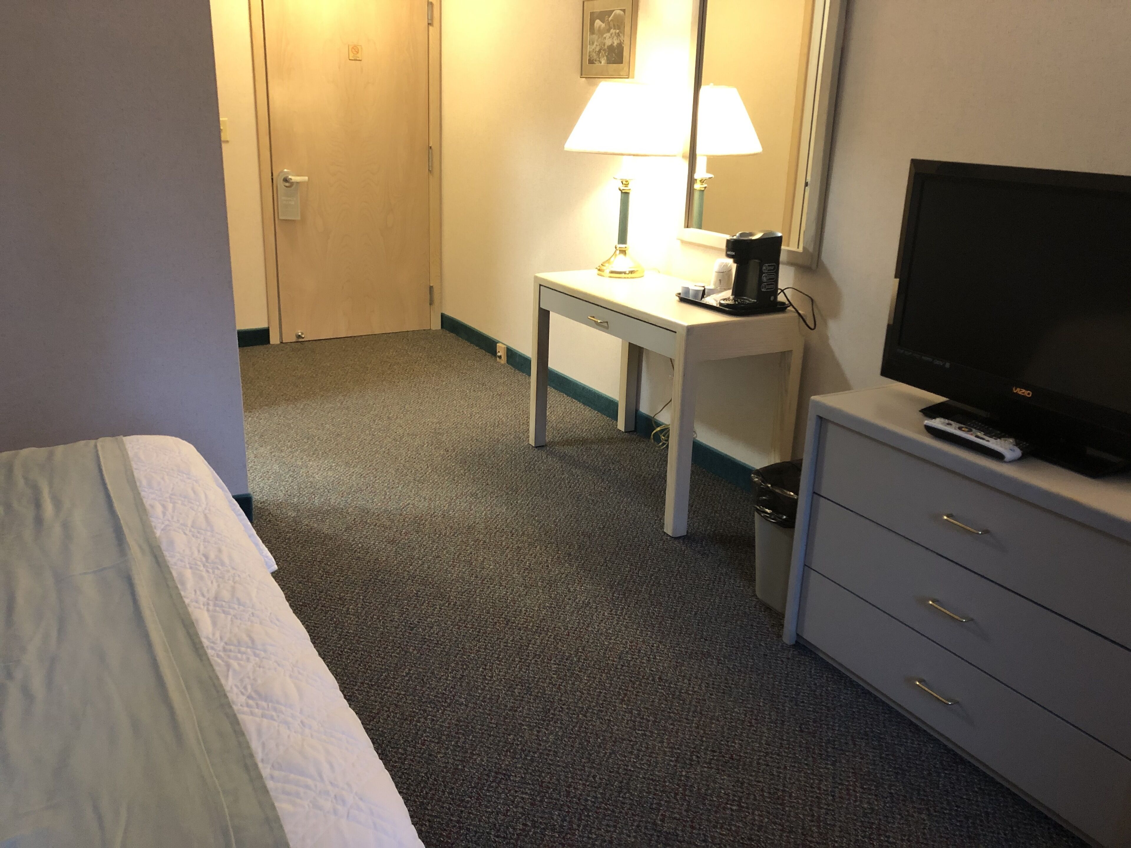 Une chambre d’hôtel avec un lit, un bureau doté d’une lampe, une télévision et une poubelle.