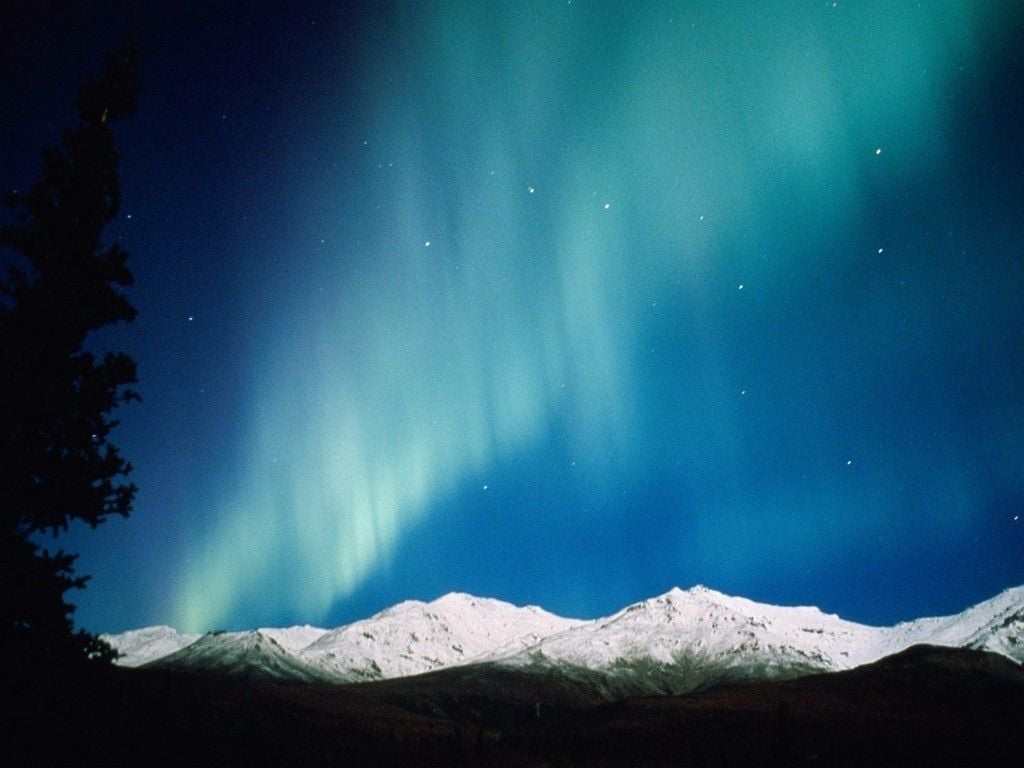 A night sky with the Northern Lights over snow-covered mountains.