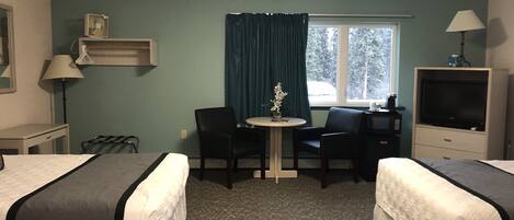 A hotel room with two beds, a desk, a chair, a small table with a vase, a TV, and a window with curtains.