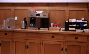 Zona cuina amb cafetera, dispensador d'aigua i prestatges amb diversos aliments.