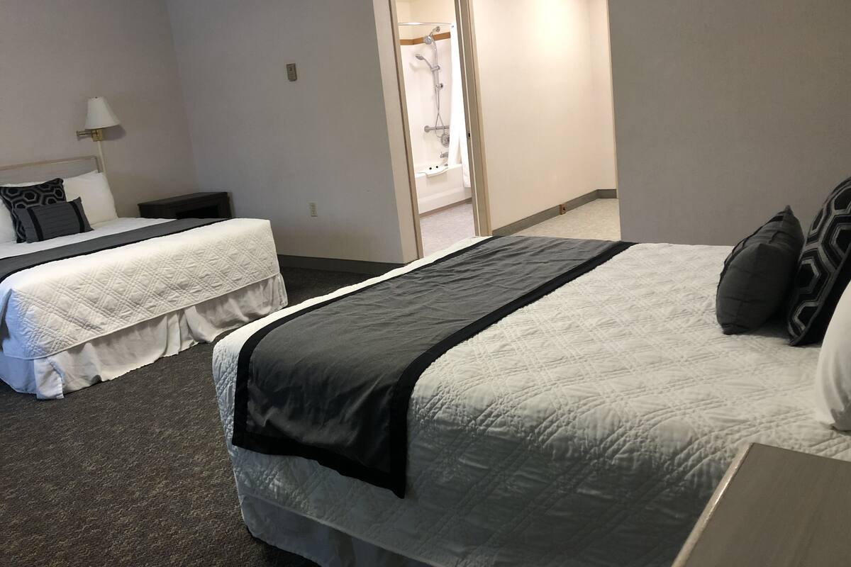 A hotel room with two beds, a nightstand, a lamp, and a shower area.