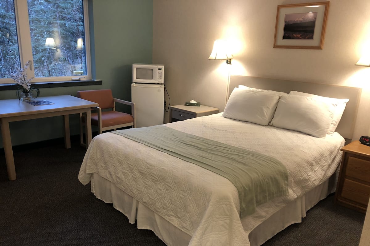 A hotel room with a bed, bedside table, lamp, and a small table with a chair.