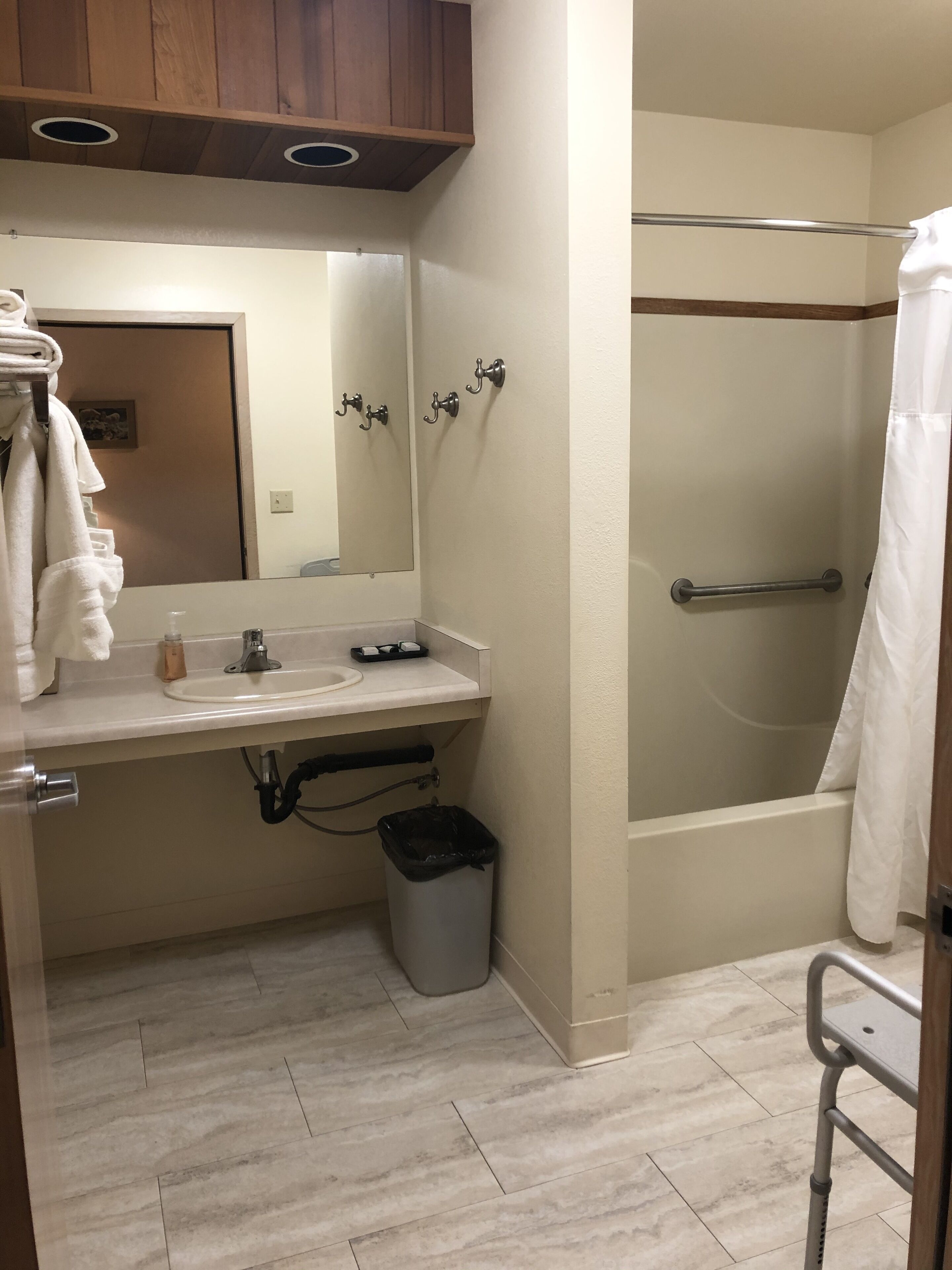 A bathroom with a sink, mirror, towel rack, shower, and a trash bin.