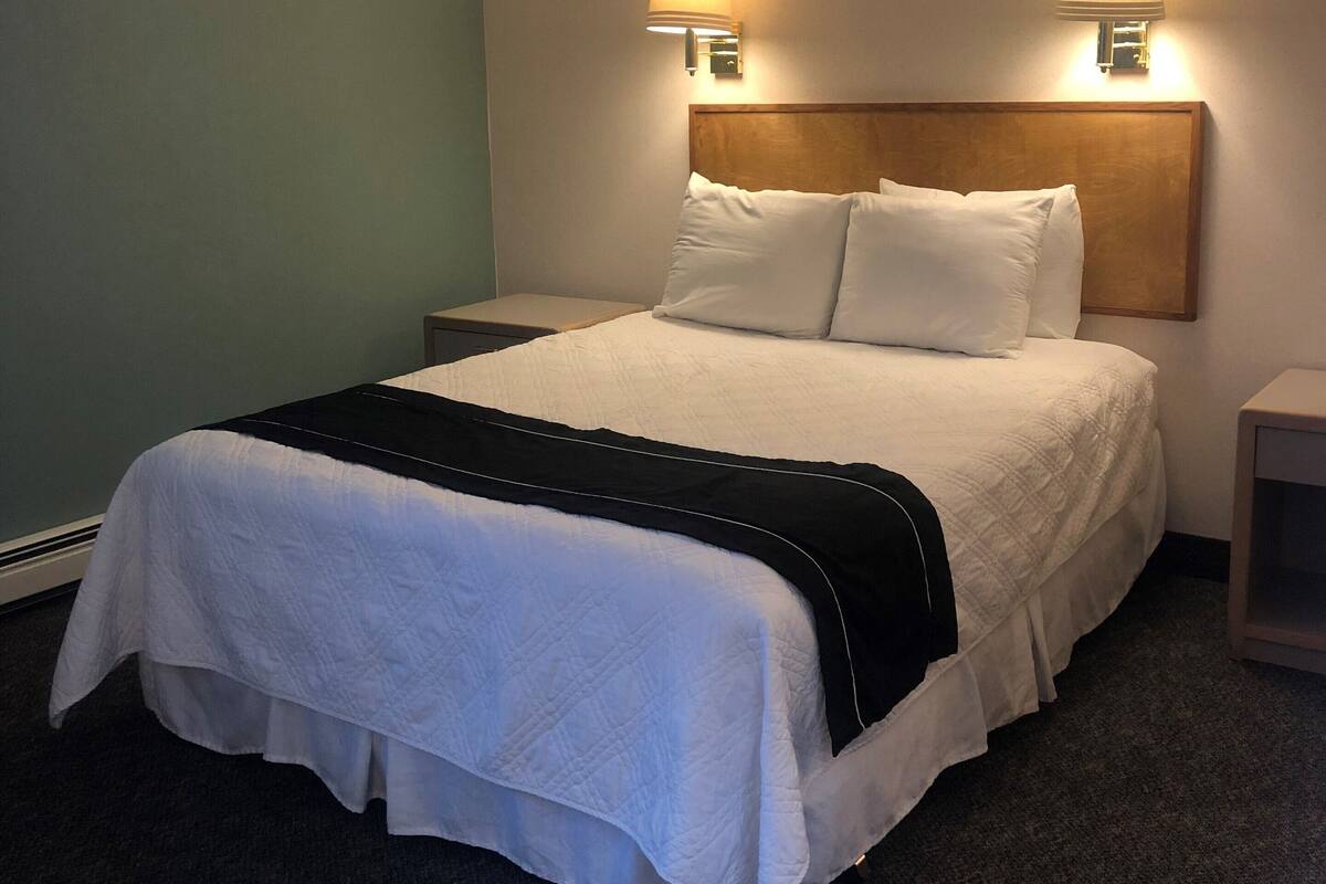 A neatly made bed with white linens and a black throw blanket, two bedside lamps, and a wooden headboard.