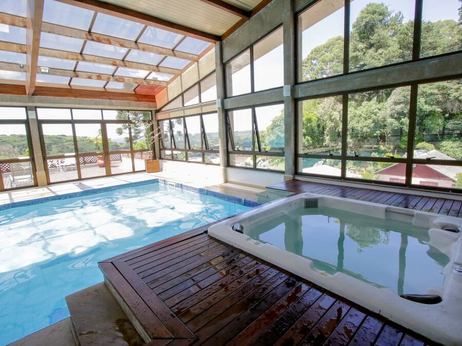 Una piscina con hidromasaje, terraza de madera y amplios ventanales que ofrecen vistas del paisaje circundante.