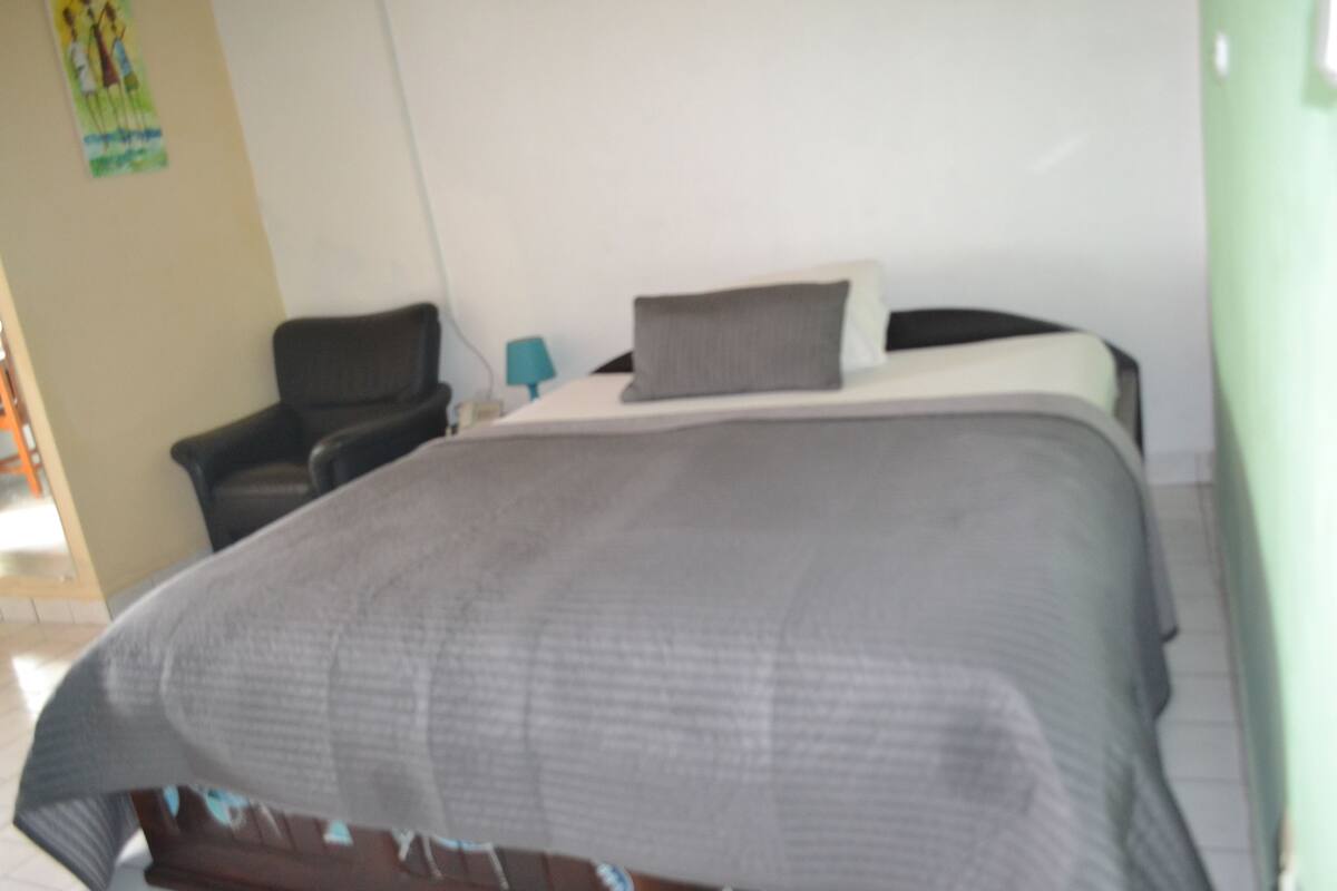A bedroom with a bed, a chair, and a nightstand.