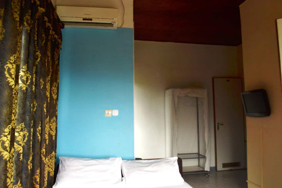 A hotel room with a bed, a blue wall, a shower area, and a television on the wall.