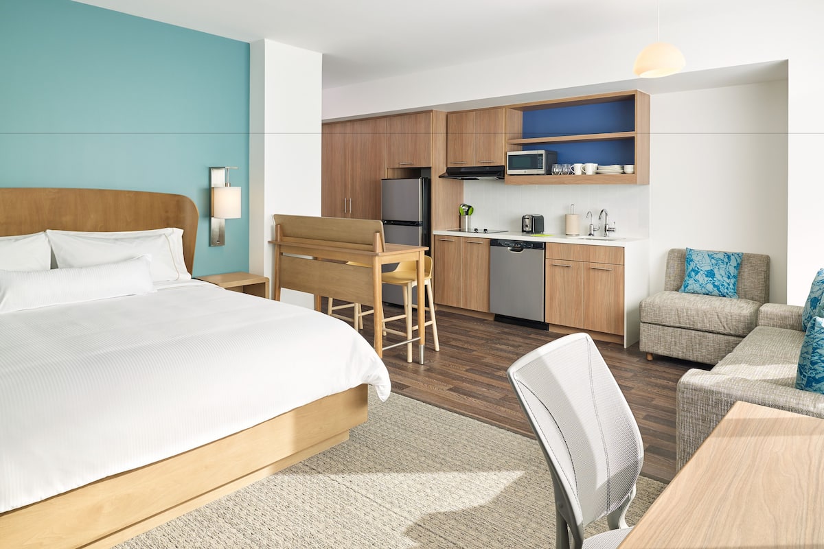 Een hotelkamer met een bed, bureau, kitchenette en zithoek.