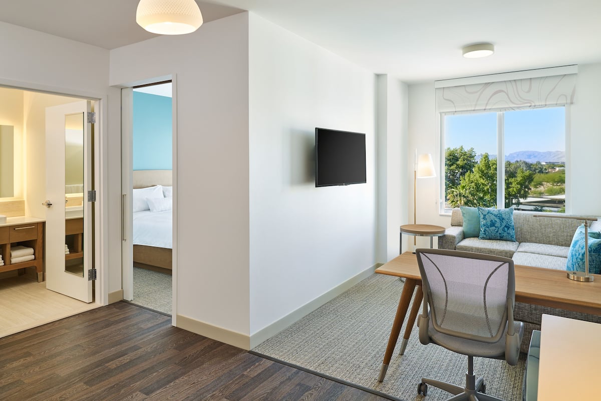 Een hotelkamer met een bed, een bureau, een stoel, een televisie en uitzicht op het omliggende landschap.