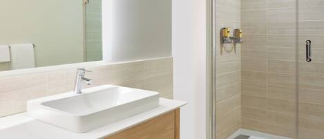A modern bathroom with a white sink, wooden vanity, and a glass-enclosed shower area.