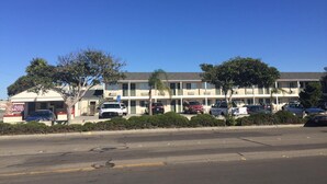 A motel with multiple-story buildings, a parking lot, and several cars parked in front. - Colonial Motel (Santa Maria)