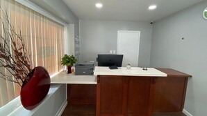 A modern office space with a wooden desk, a computer, and a vase of flowers. - Colonial Motel (Santa Maria)