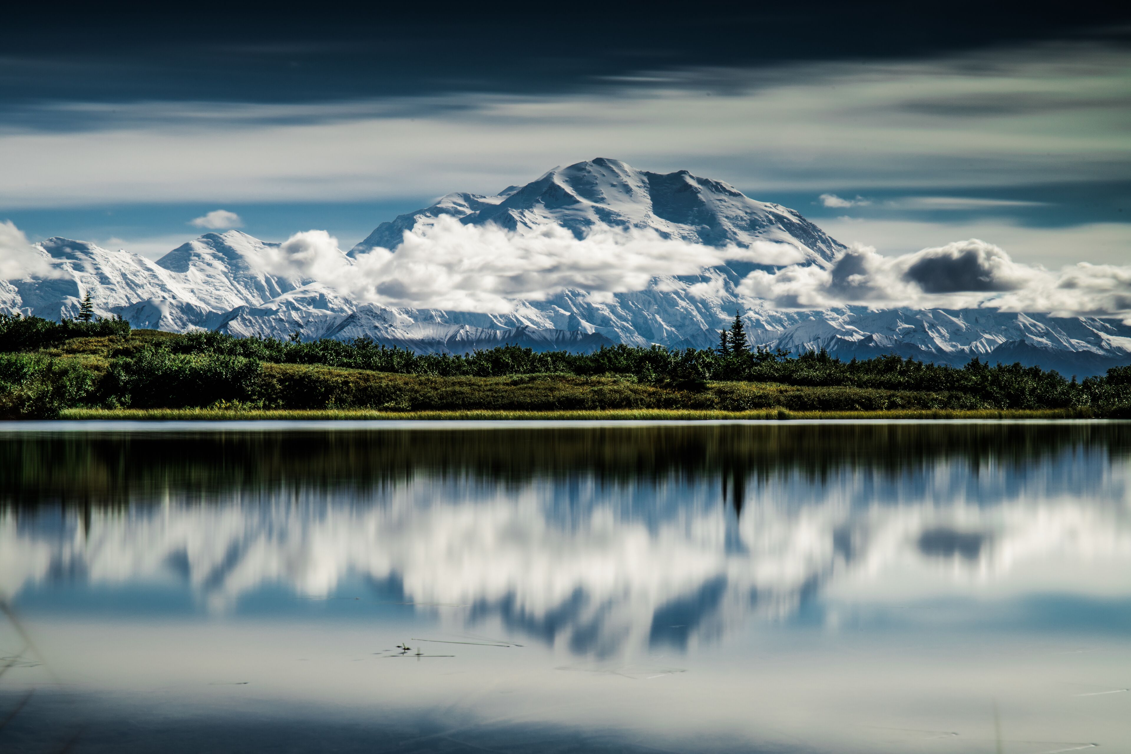 Une chaîne de montagnes aux sommets enneigés et un lac paisible qui reflète le paysage.