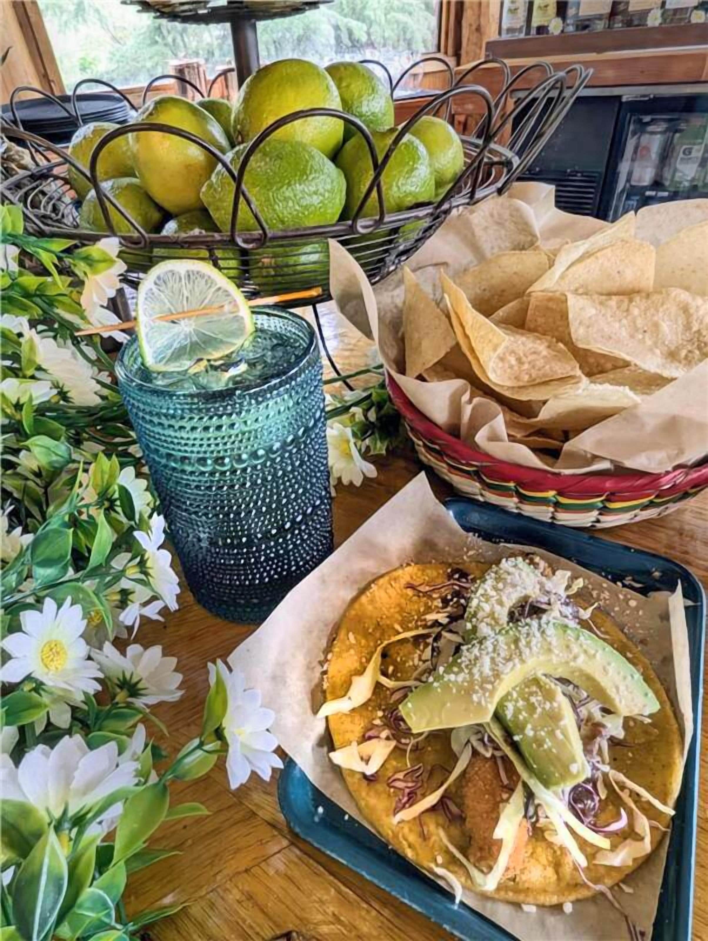 A table with a blue glass, a basket of chips, and a plate of food.