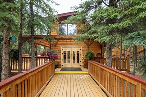 A wooden deck leading to a cabin with a large door and windows, surrounded by trees.