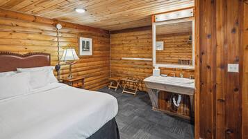 A wooden cabin-style room with a bed, a bedside lamp, a mirror, and a sink.