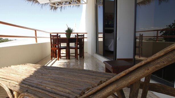 Una poltrona da lounge in legno su un balcone, con un tavolino e sedie, una pianta in vaso e vista sul panorama.