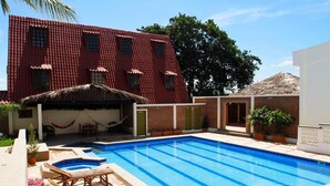 Una piscina con una struttura a tetto di paglia, un edificio in mattoni e piante in vaso.