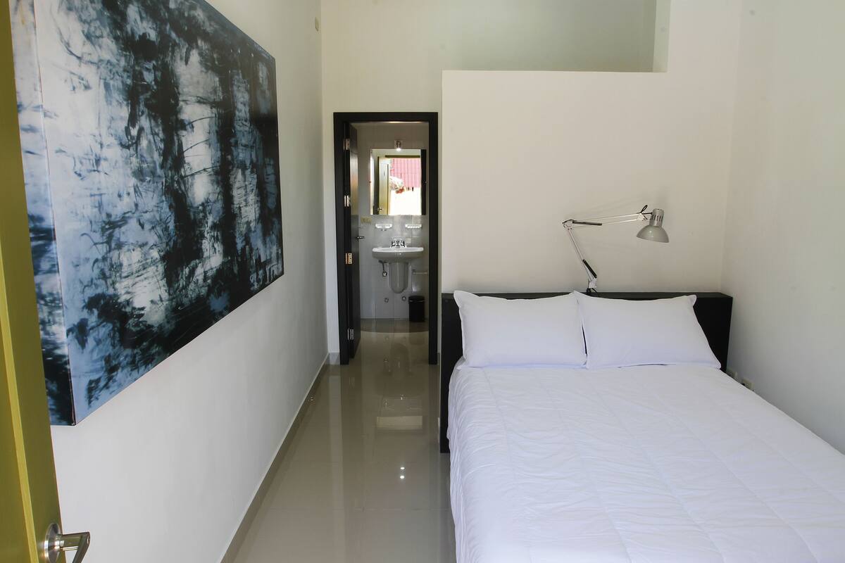 Habitación de hotel con cama, lámpara de noche, un cuadro abstracto grande en la pared y vistas al baño.