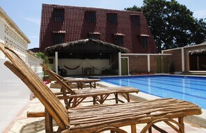 Un área de piscina con sillones reclinables y un edificio con tejado de azulejos al fondo.